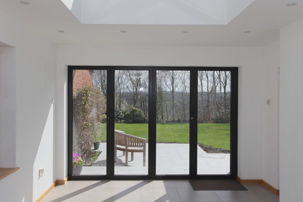 4 pane bifold doors set in white walls leading out to a patio and lawn